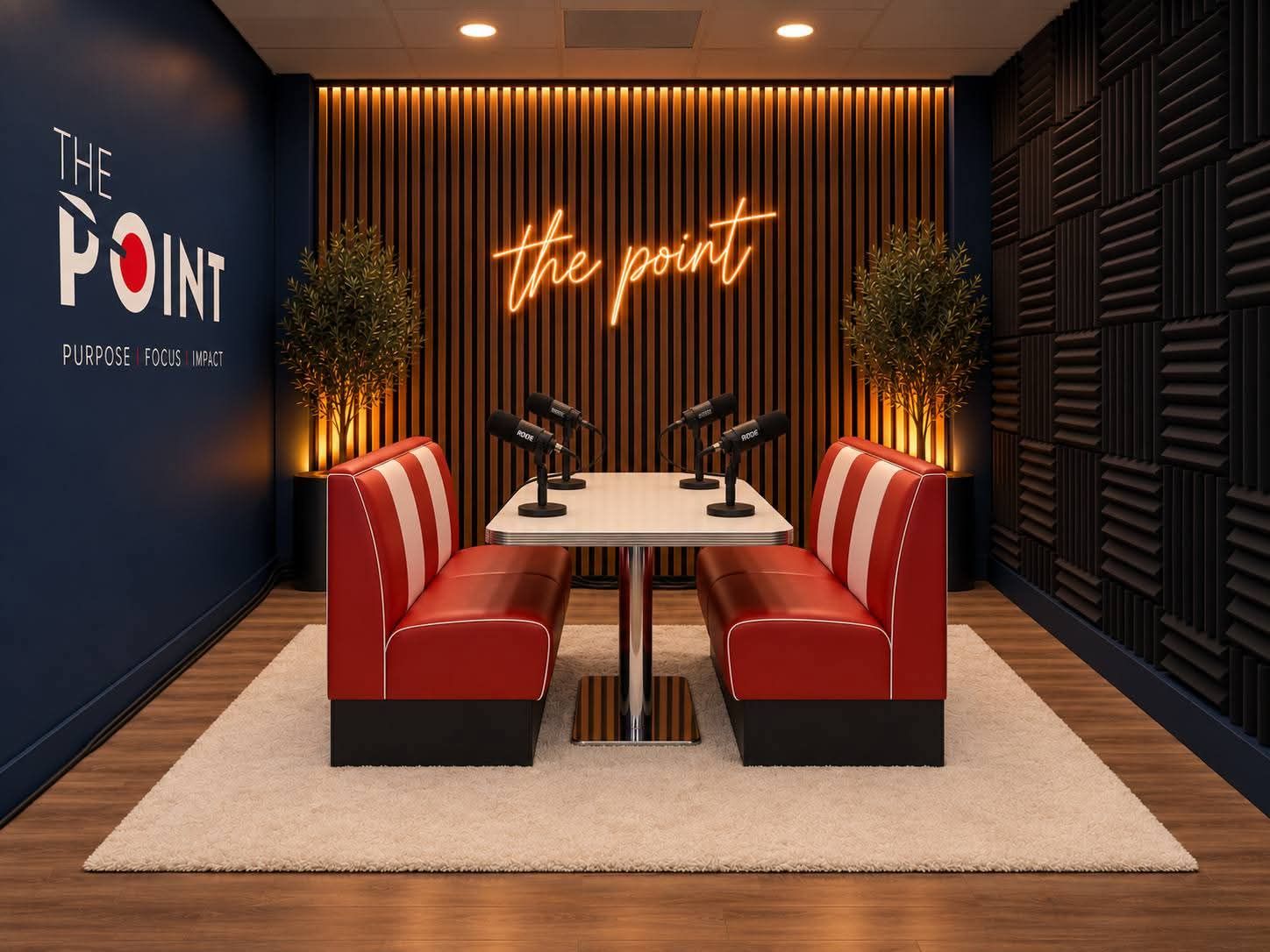 The Point podcast studio: red diner-style booth with four Rode microphones, wood slat wall and an orange neon 'the point' sign